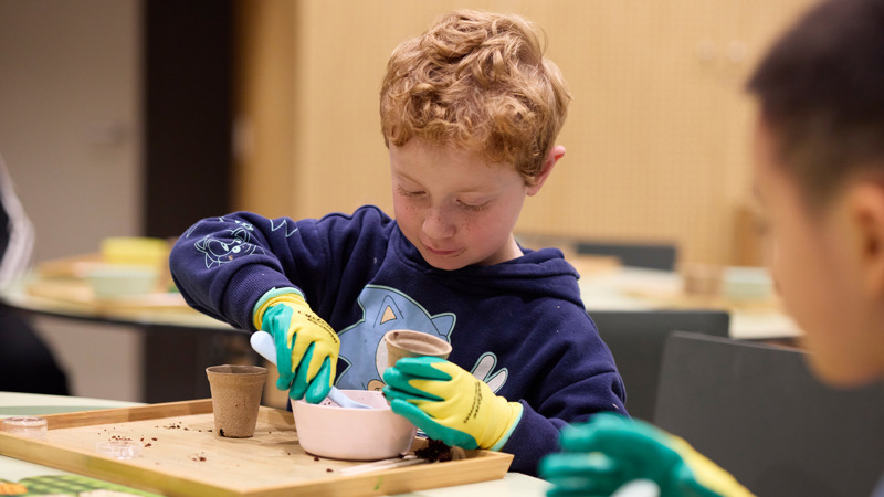 Child wearing gardening gloves scooping dirt into a pot. 