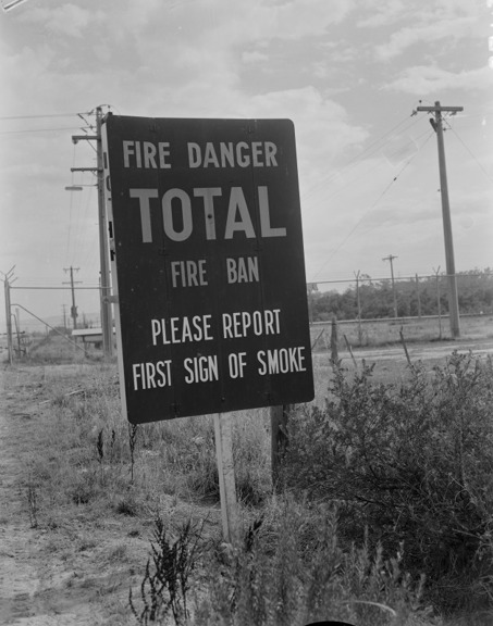 A greyscale image of a fire sign that reads " Fire Danger - Total Fire Ban Please Report First Sign of Smoke"