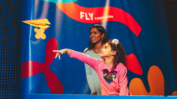 A girl throws a paper airplane across the air vents of float exhibition.