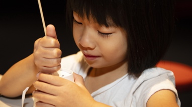 A young girl uses a skewer to poke holes in the top of her constellation cup