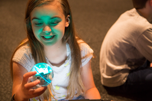 A child holds a blue glowing sphero robot.