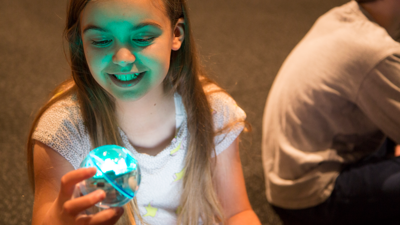 A child holds a blue glowing sphero robot.