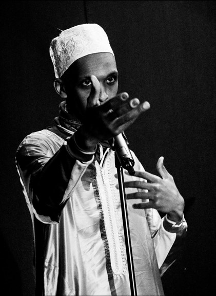 A black-and-white image of Mohamed performing with a microphone, gesturing with his hand.