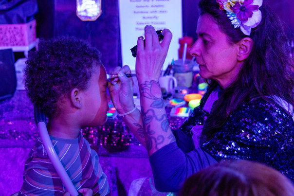 Child getting UV Face Painting in the Illuminate exhibition, during the 'Little Kids Day In - Ready, Set, Glow' event at Scienceworks.