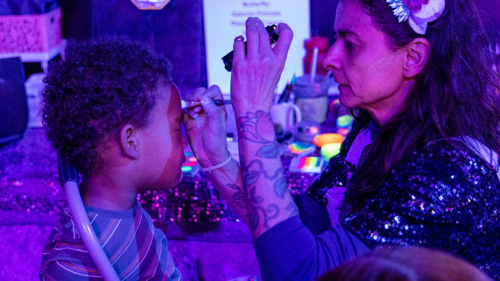 Child getting UV Face Painting in the Illuminate exhibition, during the 'Little Kids Day In - Ready, Set, Glow' event at Scienceworks.