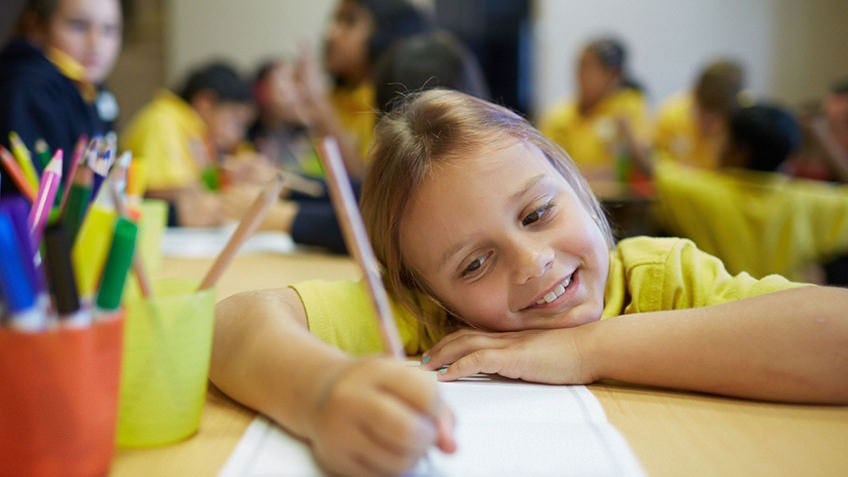 A smiling girl illustrates a page in a book she is making.