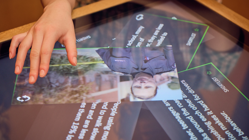 A touch table screen in the Road to Zero Learning Studio with image and text cards being moved by a student’s hand 