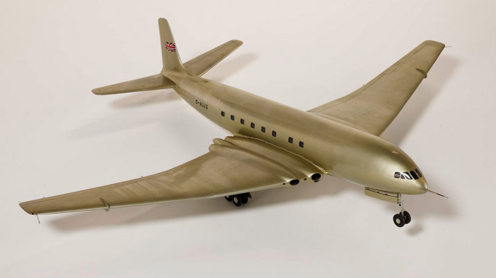 Silver model aeroplane, four wheels beneath each wing and two front wheels. British flag painted on tail.