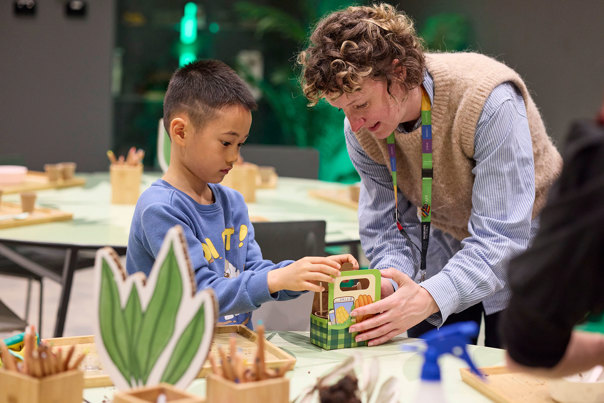 A programs officer helps a small child learn about potting seeds during Seed Stories workshop at Melbourne Museum.