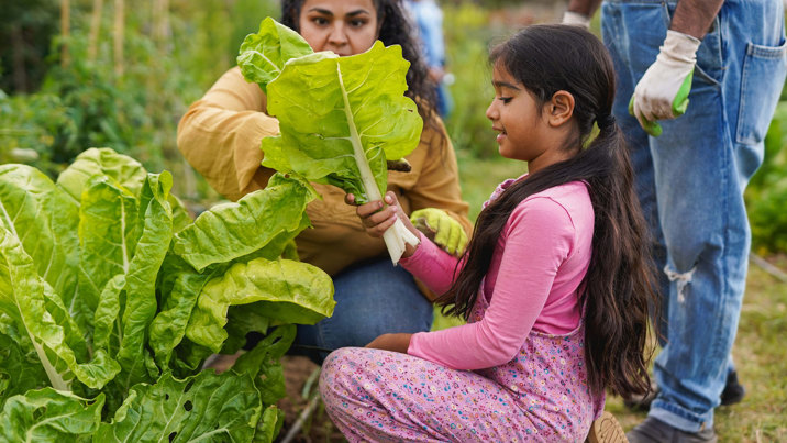 A young woman crouches with a bundle of spinach