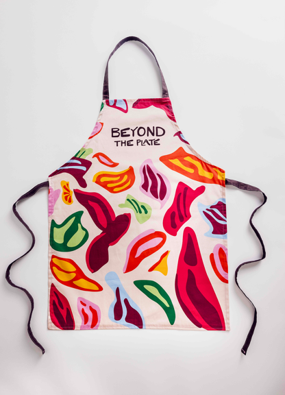 Apron with a colourful abstract pattern and black neck and waist ties, featuring the text "BEYOND THE PLATE" in bold black letters.