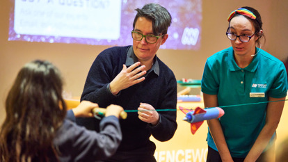 A student holds a rocket on a rope getting ready for it to launch. A Scienceworks presenter and a teacher are watching on. 