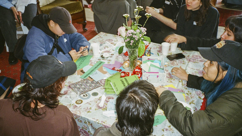 A group of young people sitting around the table with activity materials and a vase with pale pink and white flowers.