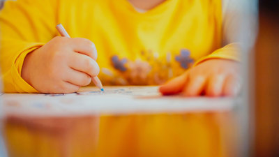 Close up of a child's hands using a coloured pencil to colour something in.