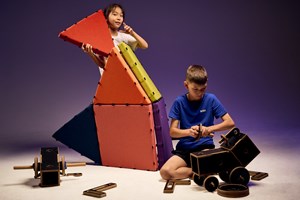 A girl standing plays with colourful magnetic cushions while a boy seated puts together loose parts with black coated plywood and dowels in Tinkertown exhibition at Scienceworks.