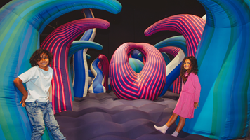 Two children pose on a a huge tentacled structure filled with air.