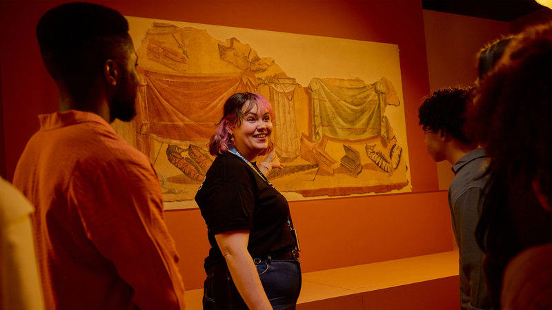 A tour guide giving a tour of the ROME: Empire, Power, People exhibition at Melbourne  Museum.