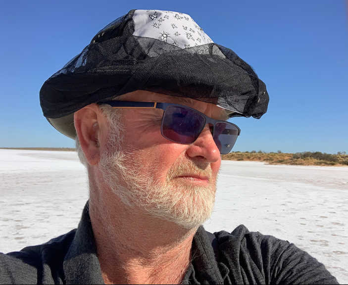 John Kean wearing a hat with fly net standing in the desert