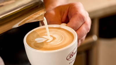 A man pouring froth onto a cappuccino. 