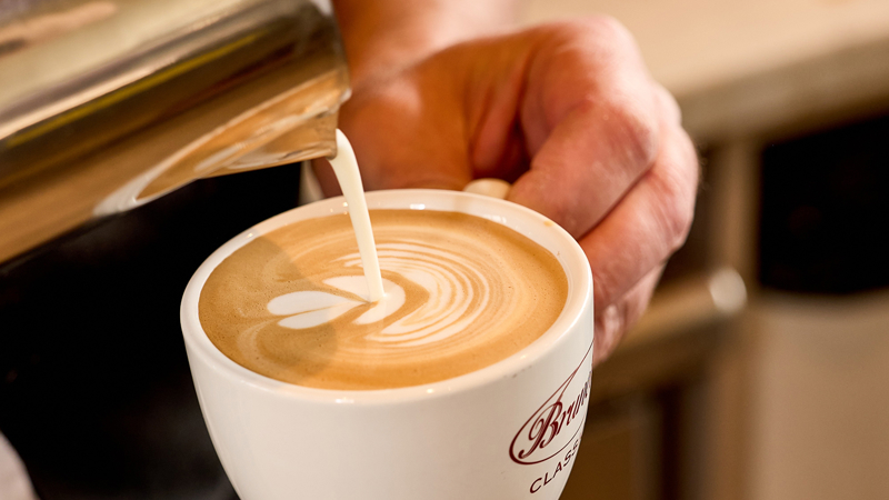 A man pouring froth onto a cappuccino. 