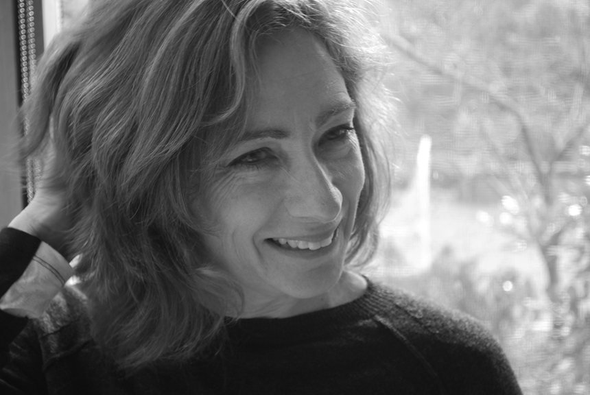 Black and white headshot of Hannah Lewi in front of a window looking onto bushland.