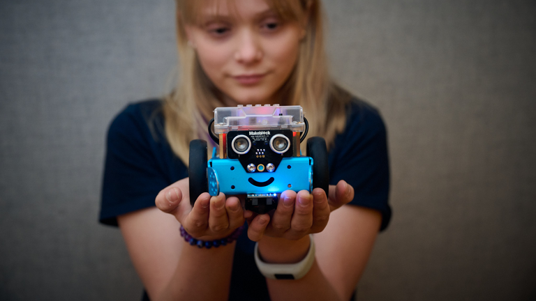 A young person poses holding a blue mBot robot