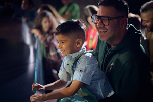 A man wearing dark rim glasses holding a child up to view and exhibit. They are both smiling
