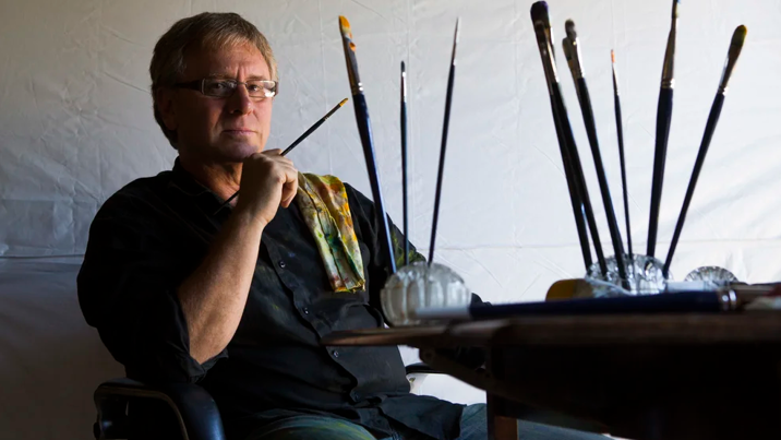 Richard Payne sits next to paints and brushes.