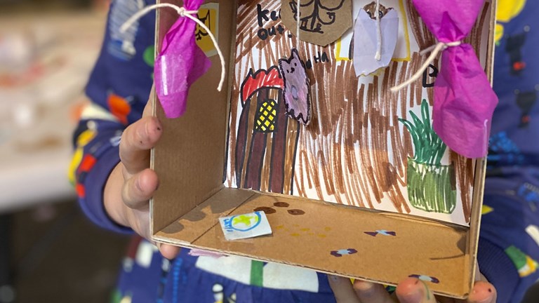 A child holds a carboard diorama they have made.
