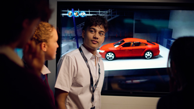 Students in the Road to Zero Experience Space standing in front of a touch screen with a red car on the screen 