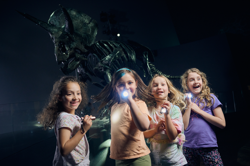 4 children with torches stand before Horridus the triceratops skeleton.
