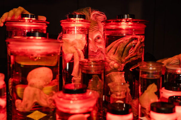 A museum expert crouches behind a wall of marine animal collections preserved in jars during Halloween at the Museum.