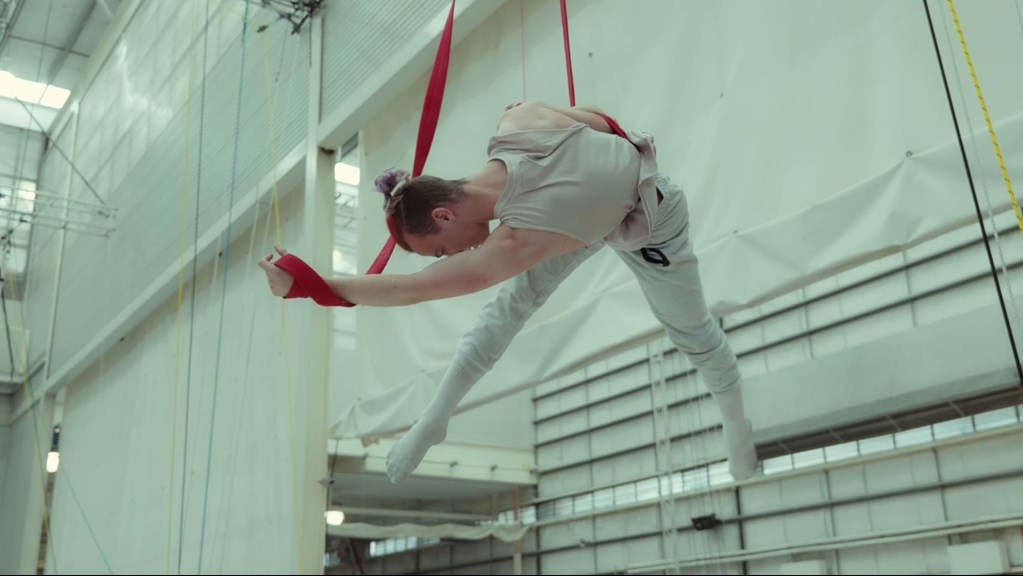 A person wearing all white, suspended mid-air holding aerial straps.