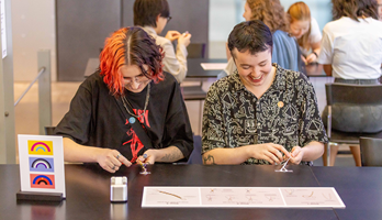 A couple of people making friendship bracelets at a crafting table activity at Nocturnal,  Melbourne Museum.