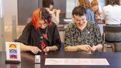 A couple of people making friendship bracelets at a crafting table activity at Nocturnal,  Melbourne Museum.