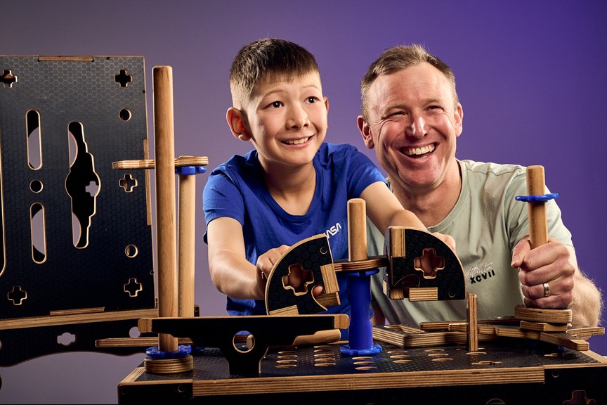 A boy and his father grip parts of a control panel constructed out of black coated plywood and blue silicone tubes in Tinkertown exhibition at Scienceworks.