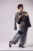 Person wears a brown tweed oversized top with sheer grey wide-leg trousers and black heels.