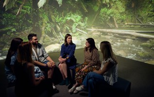 A group of people sitting in a circle having a discussion. A large image of a forest covers the wall in the background.