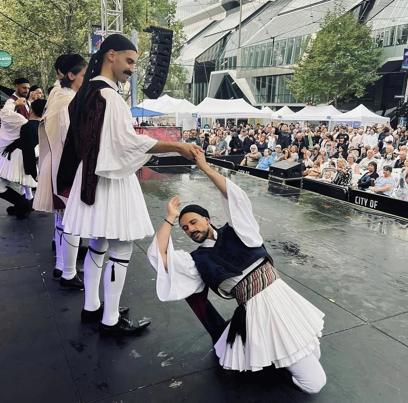 Greek dancers in traditional white outfits dancing on a stage.