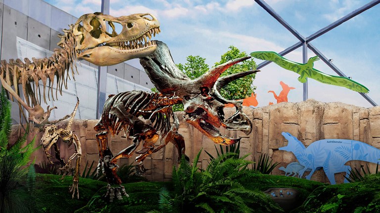 Dinosaur skeletons and lush vegetation transposed over a view of Gandel Gondwana Garden at Melbourne Museum