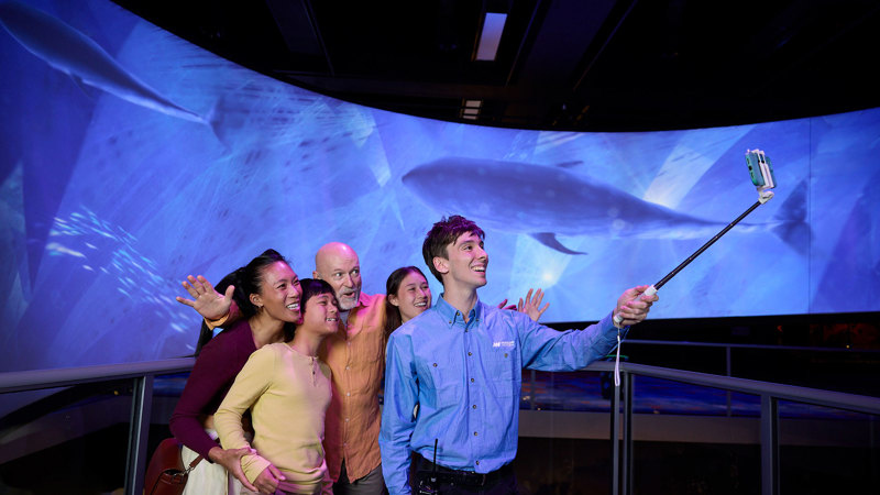 A tour guide using a selfie stick with a family touring Our Wondrous Planet exhibition at Melbourne Museum.