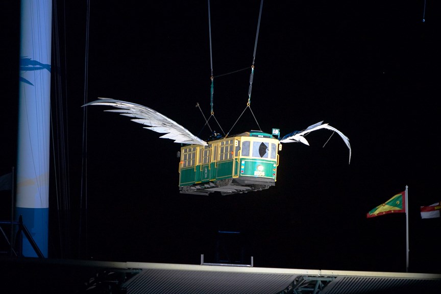 A green and yellow tram with wings, hovering above a stadium