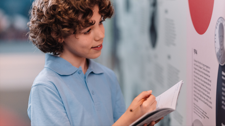 Child filling in a student booklet in the Voices Across Time gallery at Immigration Museum on a school excursion.