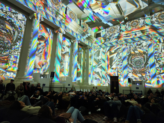People watching a lightshow projected on the walls of the Long Room at the Immigration Museum.