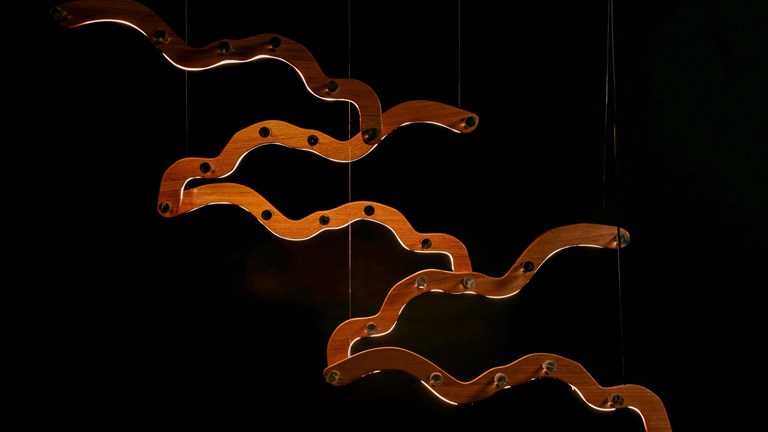 Suspended light feature with sculptural, undulating wood components.