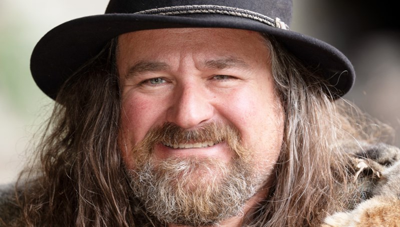 Close up portrait of man with long hair and beard wearing a hat smiling