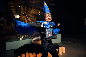 A boy dressed as a wizard jumps for joy in front of the Melbourne Museum's whale skeleton.