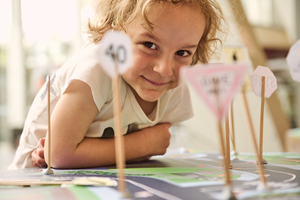 A child is smiling next to the miniature road signs they have created and added to a vinyl road map.