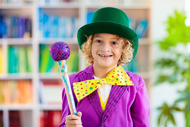 Child dressed as Willy Wonka with bright purple suit with green hat and yellow polka dot bow tie with walking stick that looks like a lollipop