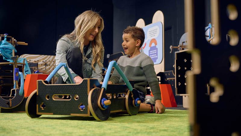 A Blonde woman and brunette boy build a wheeled contraption in Tinkertown